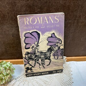 May include: A vintage paperback book titled "Romans" by Walter R. Fee and Violet Fee. The cover features a purple and white illustration of Roman soldiers riding horses and a chariot. The book is a Unit Study Book No. 405.