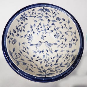 May include: A white ceramic bowl with a blue and white floral design and two birds. The bowl has a blue rim with white dots.