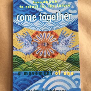 May include: Book cover with a blue, yellow, and green illustration of two birds facing each other. The title is "come together" and the subtitle is "a movement of one". The author is "dana simson & the thinkers gang".
