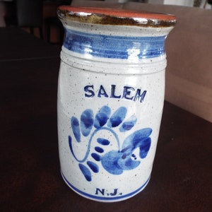 May include: White ceramic jar with blue and brown accents. The jar has a blue floral design and the words "SALEM N.J." on the front.