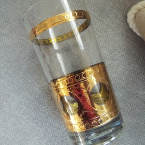 May include: A clear glass tumbler with a gold band and a gold design around the bottom. The design features circles and a pattern of small dots.