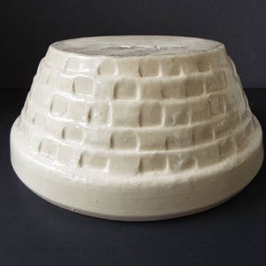 May include: A white ceramic bowl with a textured, brick-like pattern on the exterior. The bowl is round and has a wide, flat base.