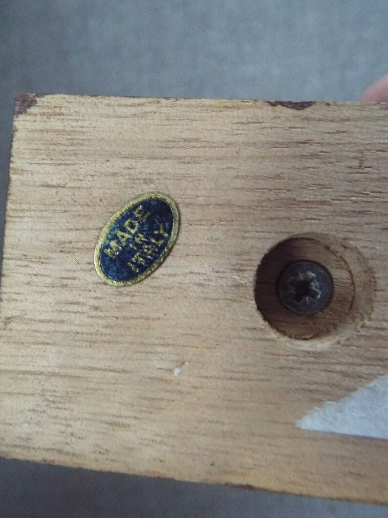 May include: Close-up of a wooden base with a blue and gold sticker that reads "Made in Italy". There is a screw in the center of the base.
