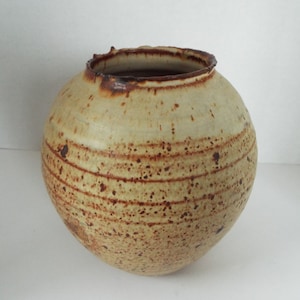 May include: A round, ceramic vase with a light brown glaze and brown speckles. The vase has a slightly uneven rim.
