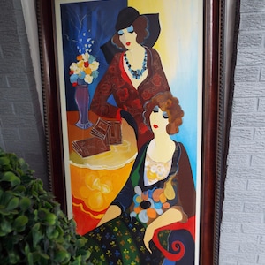 May include: An original framed painting featuring two figures in a stylized art deco style. The artwork showcases a vibrant color palette with figures adorned in patterned clothing, set against a backdrop of blue, yellow, and orange hues. The painting is enclosed in a dark brown wooden frame.