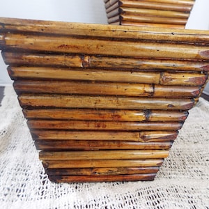 May include: Two brown woven bamboo baskets with a square shape. The baskets are made of thin strips of bamboo that are woven together to create a geometric pattern.