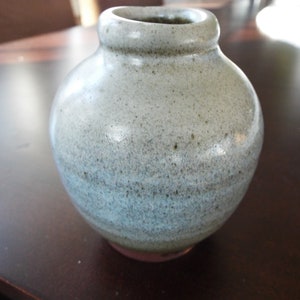 May include: A small, round, gray ceramic vase with a speckled glaze. The vase has a light blue and gray color gradient.