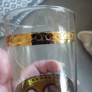 May include: A clear glass drinking glass with a gold band around the middle. The band has a repeating pattern of circles.