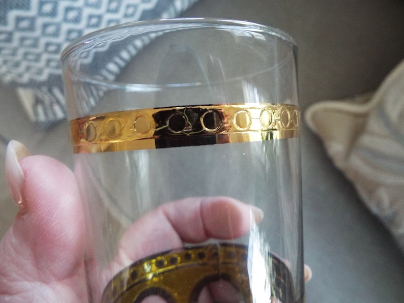 May include: A clear glass drinking glass with a gold band around the middle. The band has a repeating pattern of circles.
