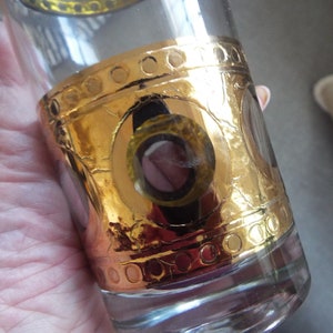 May include: A clear glass tumbler with a gold band and circular design. The gold band has a textured, hammered look.