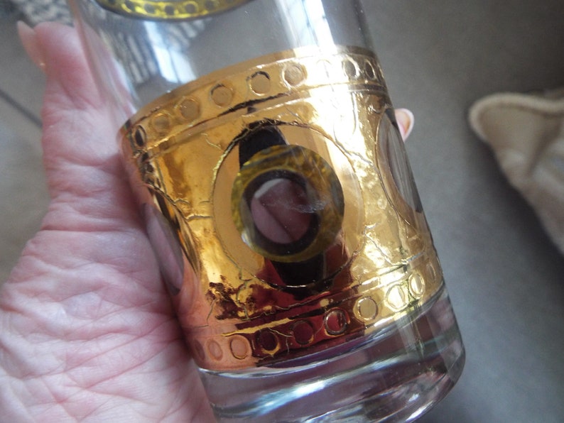 May include: A clear glass tumbler with a gold band and circular design. The gold band has a textured, hammered look.