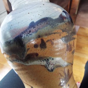 May include: A ceramic vase with a brown, white, and blue glaze. The vase has a textured surface and a unique, abstract design.