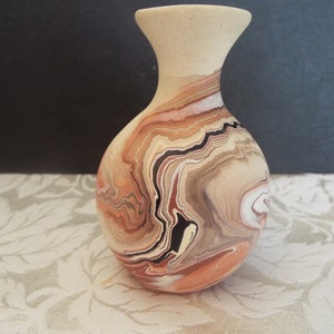 May include: A small, hand-painted ceramic vase with a marbled design in shades of brown, orange, white, and black. The vase has a rounded body and a narrow neck.