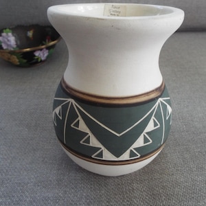 May include: White ceramic vase with a green, brown, and white geometric design. The vase has a wide mouth and a rounded body.