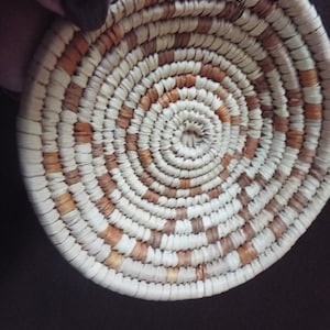 May include: A small, round woven basket with a white and brown pattern. The basket is made of natural materials and has a circular shape.