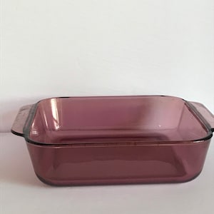 Puede incluir: Un molde para hornear cuadrado de vidrio morado con dos asas.