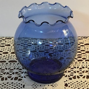 May include: A cobalt blue glass vase with a scalloped rim. The vase has a round body and a flared base.