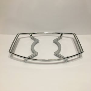 Puede incluir: Un soporte para placa caliente de metal plateado con un diseño curvo. El soporte tiene dos secciones elevadas en el medio.