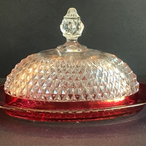 Può includere: Un porta burro in vetro vintage con un coperchio trasparente a forma di diamante e una base rossa. Il coperchio ha un pomello in vetro trasparente.