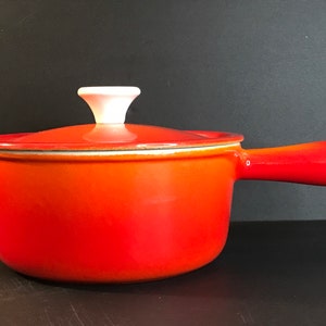 May include: Orange enamelled cast iron saucepan with a white lid knob and a red handle.