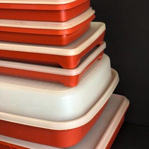 Op de afbeelding: Een set van zes rode en witte plastic opbergcontainers met deksels. De containers zijn op elkaar gestapeld, met de grootste container onderaan en de kleinste bovenaan.