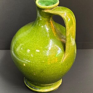 May include: A green ceramic pitcher with a rounded body, a curved handle, and a spout. The pitcher has a glossy finish and a base. The color is a vibrant, bright green.