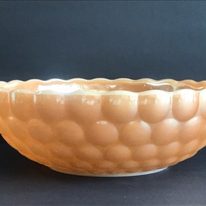 以下が含まれることがあります： 泡のようなテクスチャのデザインが施された、大きなピーチ色のガラスボウル。ボウルは丸く、わずかに波打った縁があります。