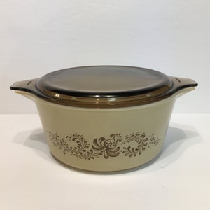 Puede incluir: Una fuente para horno marrón y beige con un diseño floral y una tapa de vidrio transparente.