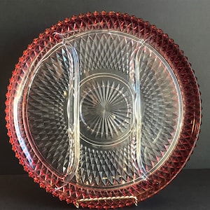 May include: A clear glass serving dish with three sections and a diamond pattern. The dish has a red rim with a diamond pattern.