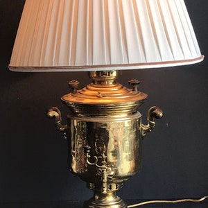 May include: A brass samovar lamp with a white pleated lampshade. The samovar has a hammered finish and a traditional design.