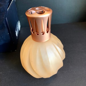 May include: A frosted glass diffuser bottle with a rose gold metal lid and decorative cutouts. The bottle has a rippled design.