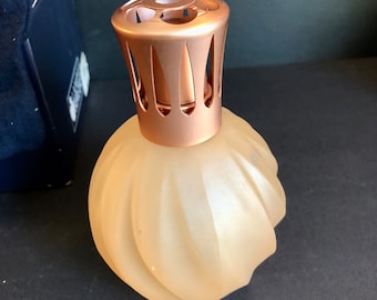 Könnte beinhalten: Eine mattierte Glasdiffusor-Flasche mit einem roségoldenen Metalldeckel und dekorativen Ausschnitten. Die Flasche hat ein geriffeltes Design.