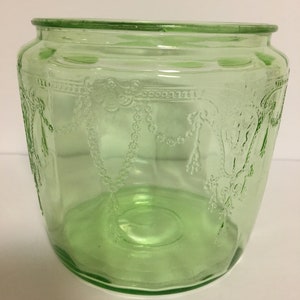 May include: A vintage green glass jar with an embossed design. The jar has a wide mouth and a rounded bottom.