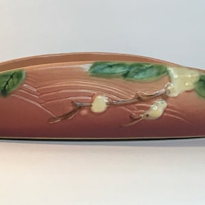 May include: A brown ceramic planter with a floral design featuring white flowers and green leaves. The planter has a curved shape and a glossy finish.