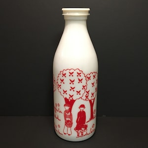 Puede incluir: Botella de leche de vidrio blanco con una ilustración roja de dos niños en un jardín con árboles. La botella tiene una tapa de plástico blanco. El diseño presenta árboles con hojas en forma de mariposa.