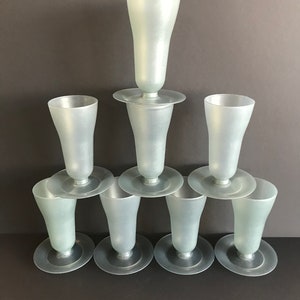 Puede incluir: Un juego de ocho vasos de plástico transparente con acabado esmerilado. Los vasos están apilados en forma de pirámide, con el vaso más grande en la parte superior y los vasos más pequeños en la parte inferior. Cada vaso tiene una base ancha y una parte superior estrecha, y todos están hechos del mismo plástico transparente.