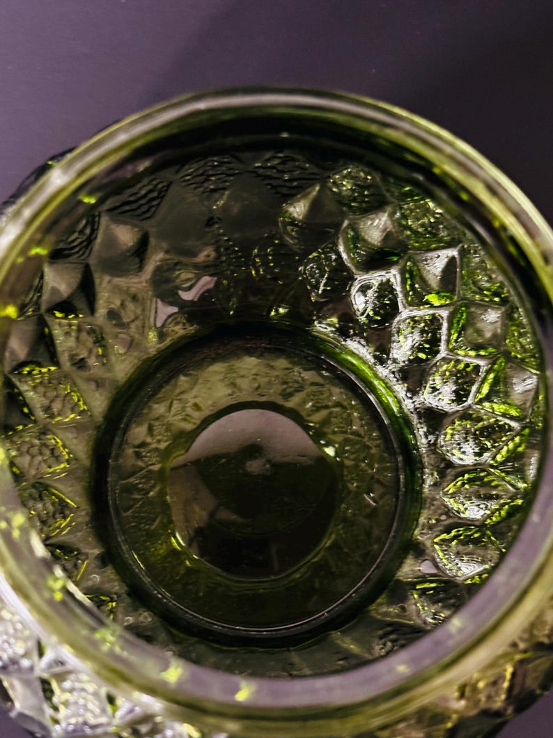 May include: Close-up of a green glass container with a textured, geometric pattern. The container has a wide opening and a thick base. The glass has a glossy finish, reflecting light and creating highlights.