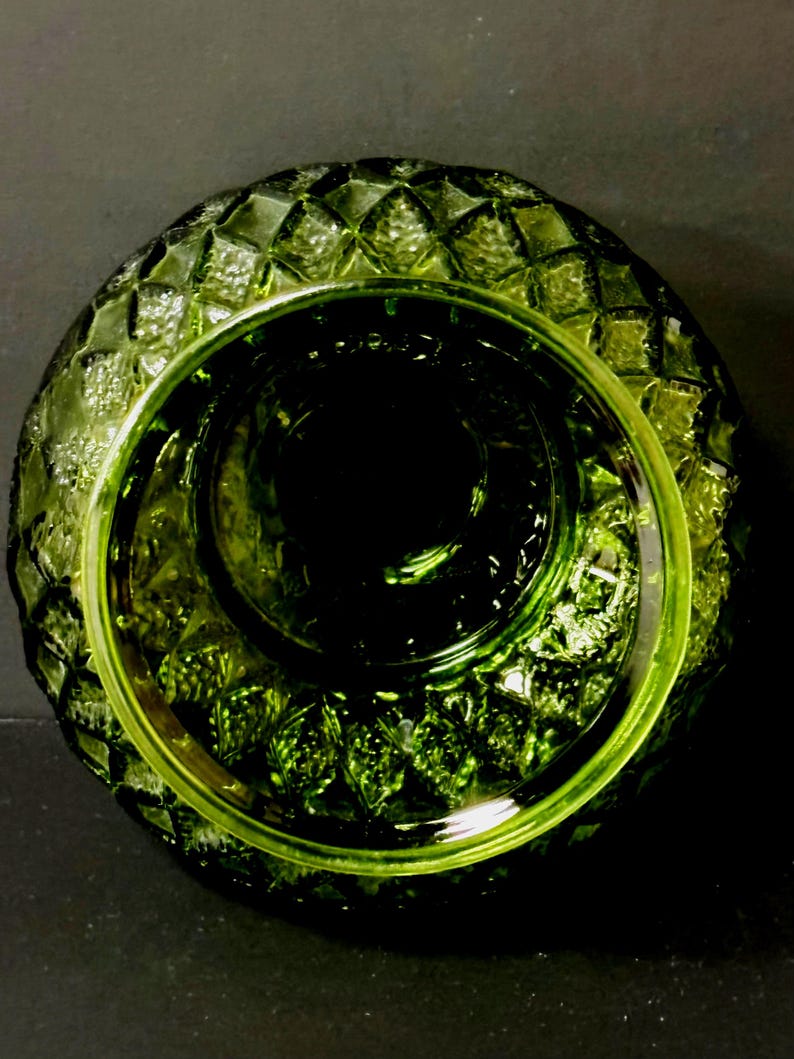May include: A top-down view of a green glass bowl with a diamond pattern around the rim. The bowl has a circular shape with a deep, dark center. The glass has a glossy finish, reflecting light and creating highlights.