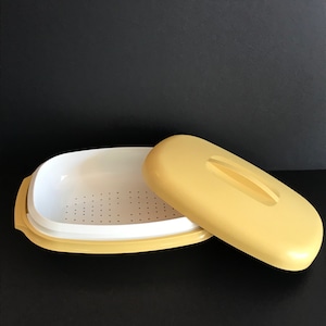 Può includere: Una vaporiera di plastica gialla con un inserto perforato bianco e un coperchio abbinato. La vaporiera è aperta e il coperchio è di lato.
