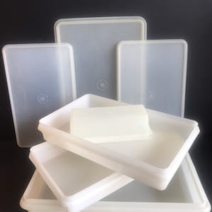 Puede incluir: Un juego de cuatro recipientes rectangulares de plástico blanco con tapas. Los recipientes están apilados uno encima del otro, con el recipiente más grande en la parte inferior y el más pequeño en la parte superior.