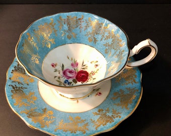 May include: A blue and gold teacup and saucer set with a floral design. The cup and saucer have a scalloped edge and are decorated with gold trim.