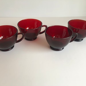 May include: Four red glass teacups with handles. The cups are all the same size and shape.