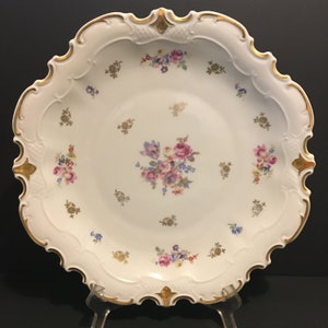 May include: A white porcelain serving dish with a scalloped edge and gold trim. The dish is decorated with a floral pattern in shades of pink, blue, and yellow.