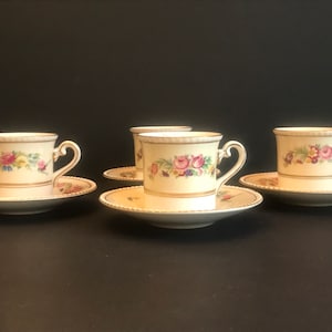 Puede incluir: Juego de cuatro tazas de té y platillos de porcelana blanca con un diseño floral. Las tazas y los platillos tienen un borde dorado y presentan un delicado patrón floral en tonos de rosa, amarillo y azul.