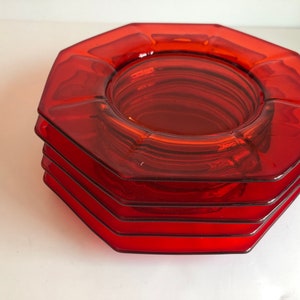 Puede incluir: Un conjunto de cuatro platos octogonales de vidrio rojo con un borde elevado. Los platos están apilados uno encima del otro, siendo el superior el más grande.