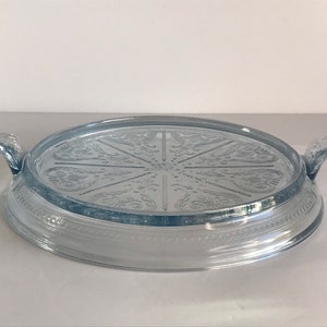 May include: A light blue glass hot pad with a decorative design and two handles.