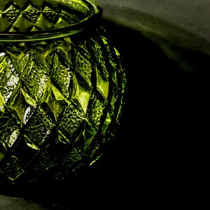 May include: A close-up of a green glass vase with a diamond pattern. The vase has a round shape with a wide opening and a textured surface. The glass reflects light, creating highlights and shadows.