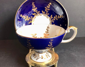 May include: A blue and gold teacup and saucer set with a floral design. The teacup has a pedestal base and the saucer has a gold rim.