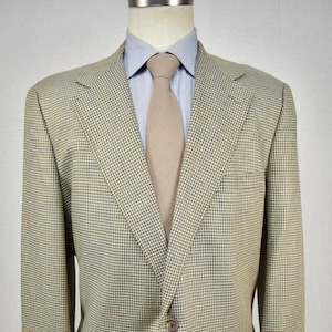May include: A tan and blue houndstooth blazer with a light blue dress shirt and a tan tie. The blazer has two front pockets and a single button closure. The jacket is displayed on a mannequin.