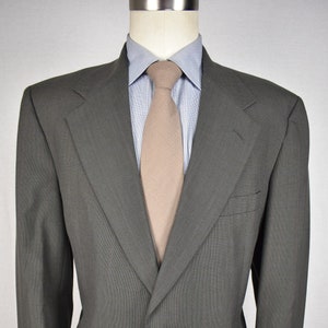 May include: A gray single-breasted blazer with a brown tie and a light blue shirt. The blazer has two buttons and a pocket on the left side.